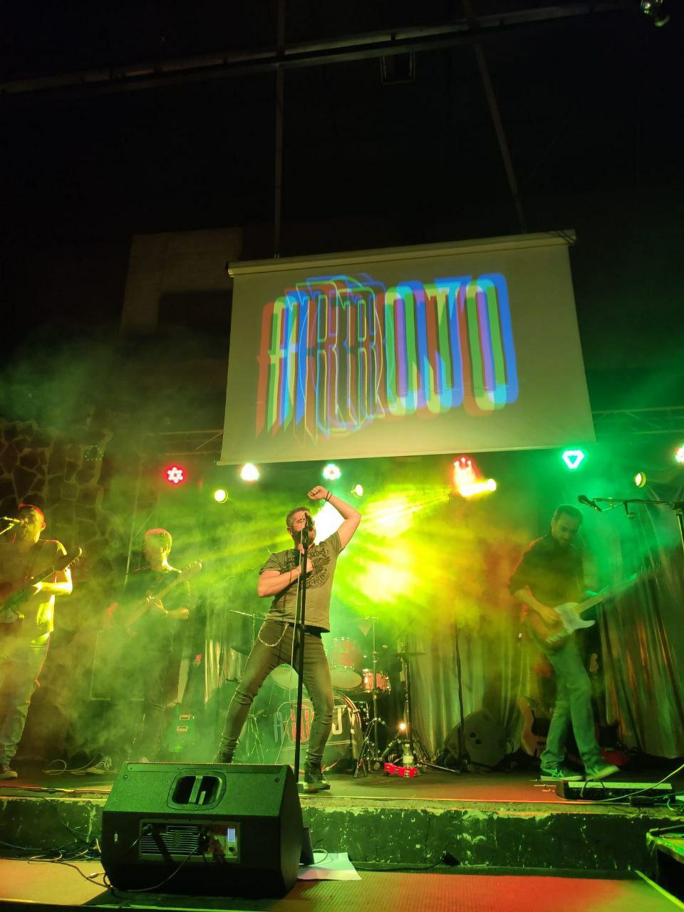 Escenario de concierto de Arrojo con luces verdes y proyección del logo de la banda