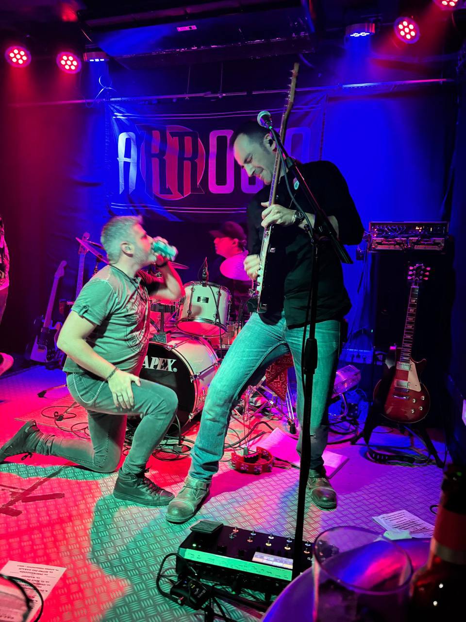 Arrojo dándolo todo en el escenario, Merino de rodillas bebiendo cerveza y Yor en pleno solo