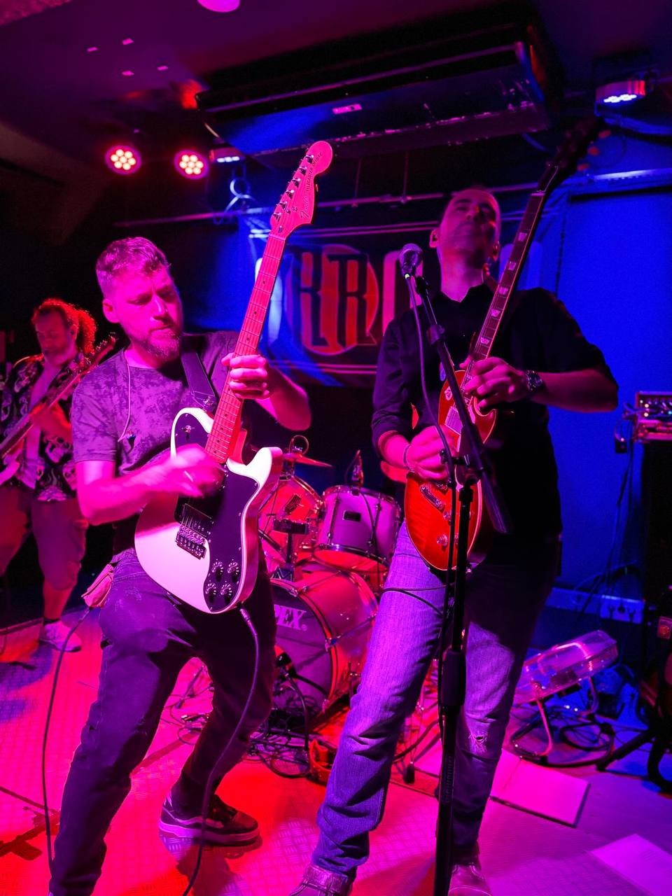 Duelo de guitarras en el escenario con potente iluminación morada