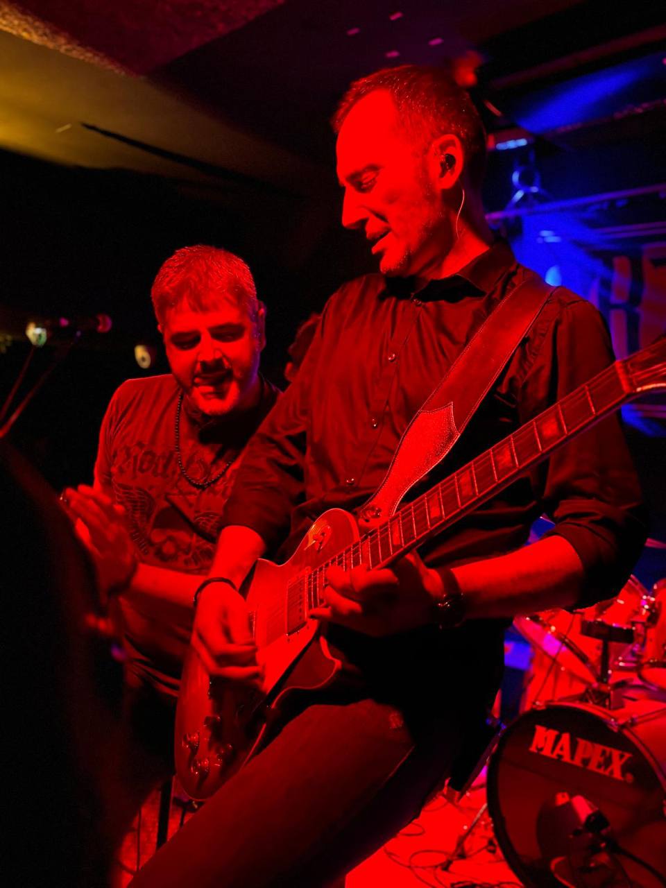 Primer plano de Yor tocando la Les Paul mientras Merino le da a la pandereta