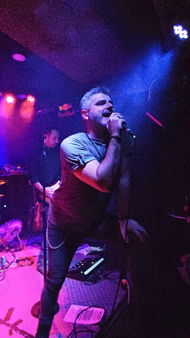 Vocalista Merino cantando con máxima pasión y fuerza bajo luz azul escénica