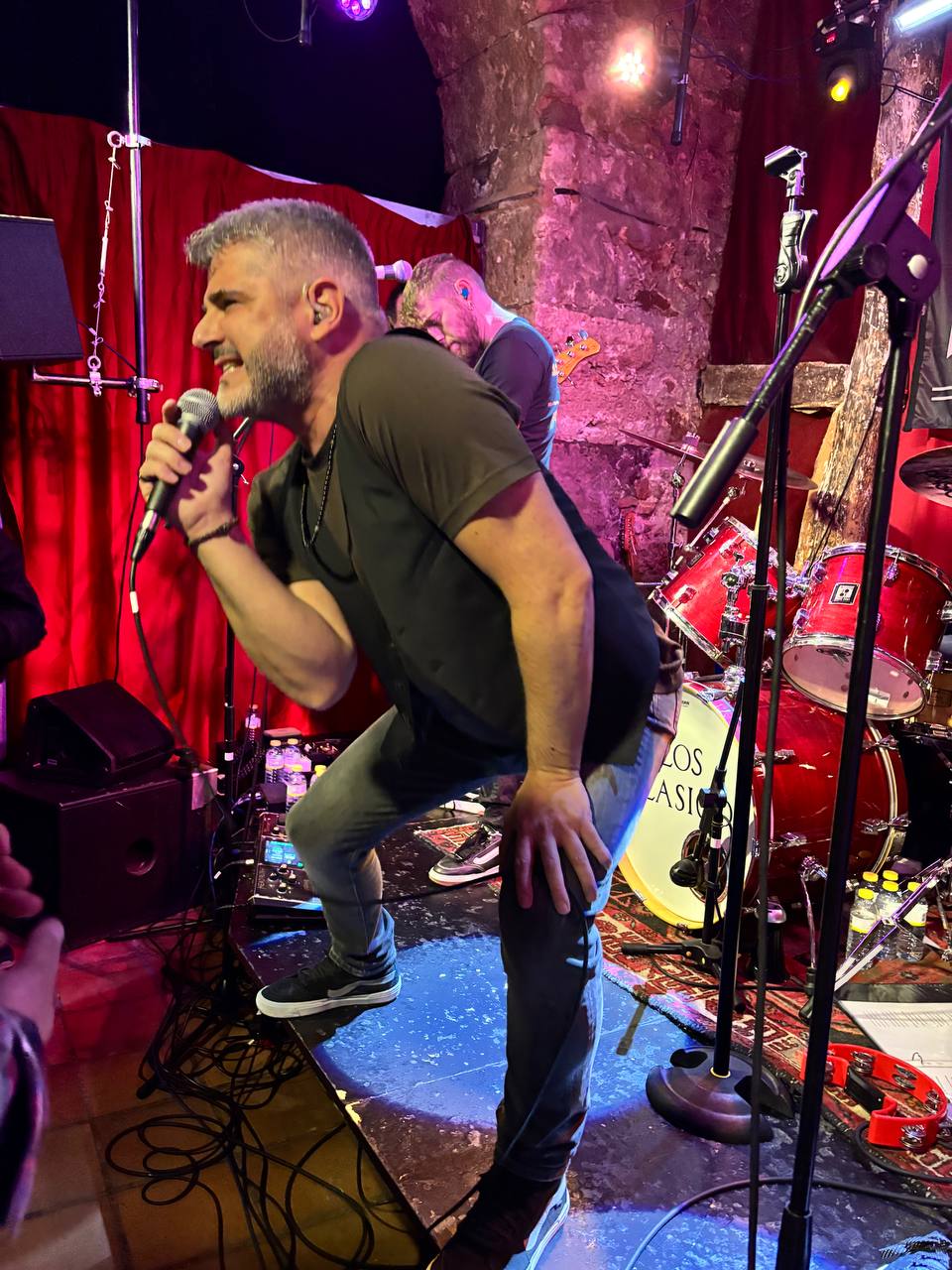 Vocalista Merino cantando con intensidad al borde del escenario con cortinas rojas de fondo