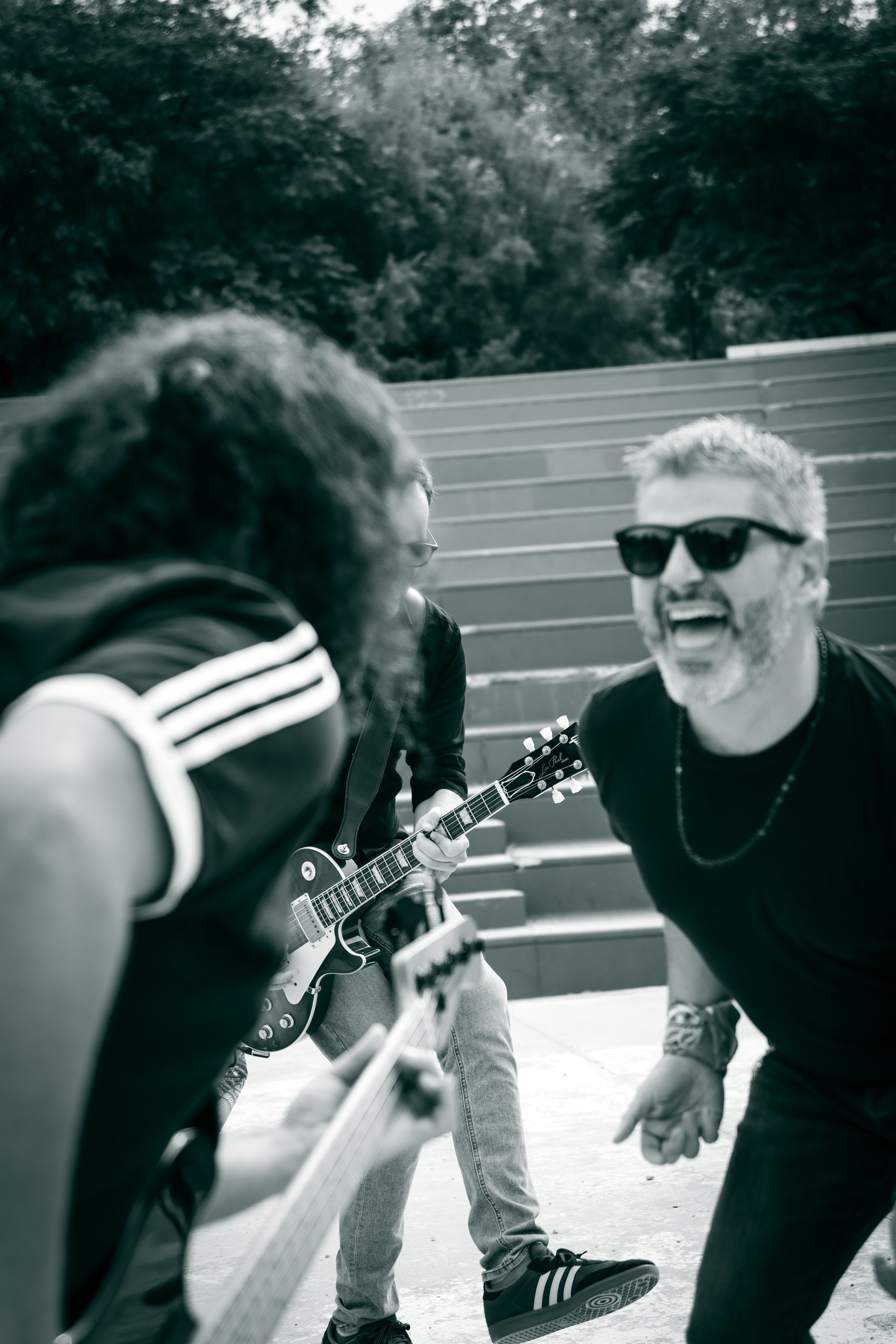 Fotografía en blanco y negro del cantante Merino riendo en primer plano con la banda tocando al fondo