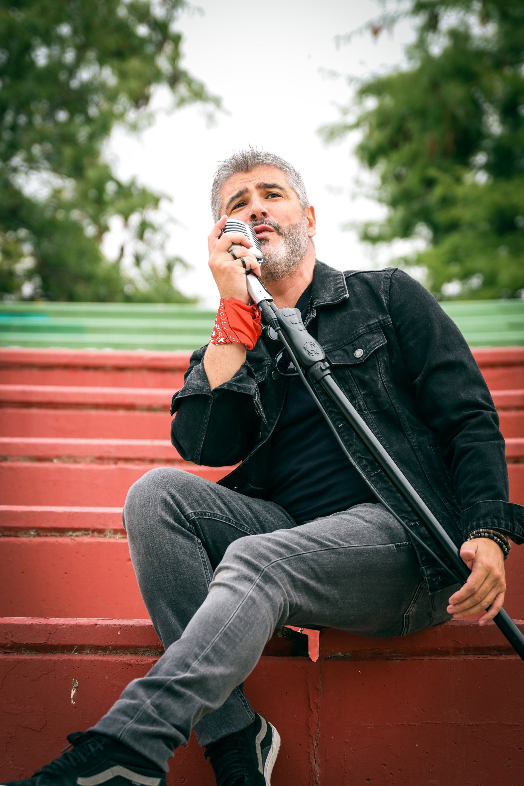 Vocalista Merino de Arrojo sentado en gradas rojas sosteniendo un micrófono clásico