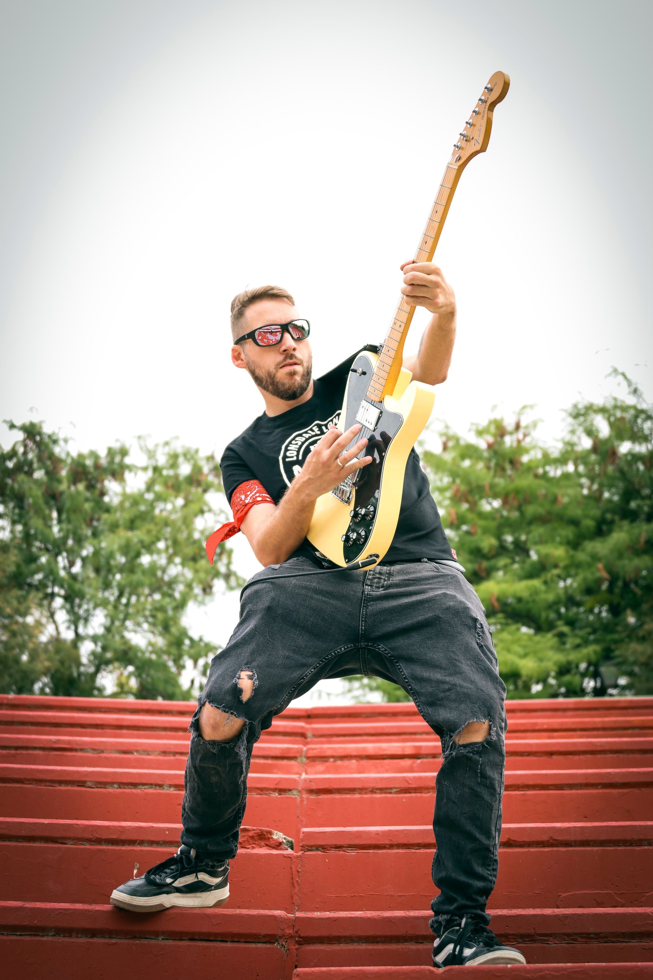 Guitarrista rítmico Guille tocando una guitarra eléctrica en postura potente sobre gradas rojas